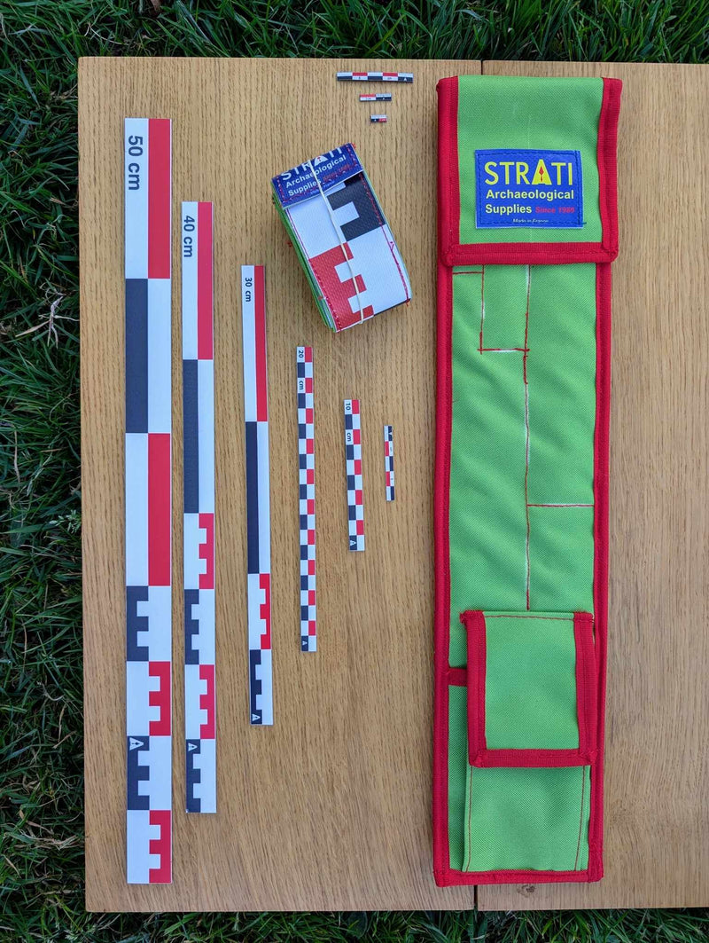 Load image into Gallery viewer, Open CAMA 50 cm canvas archaeological scale kit with green red case and red white black metric rulers on wood and grass