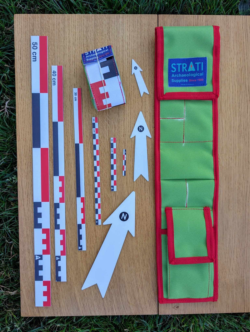 Load image into Gallery viewer, Open CANO 50 cm canvas archaeological scale kit with green red case, metric rulers and white north arrows on wood and grass