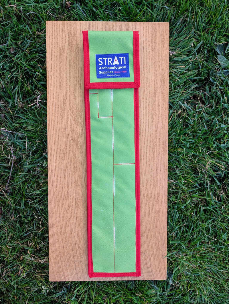 Load image into Gallery viewer, Closed green and red STRATI CASE carrying case for archaeological photo scales on a wooden board over grass