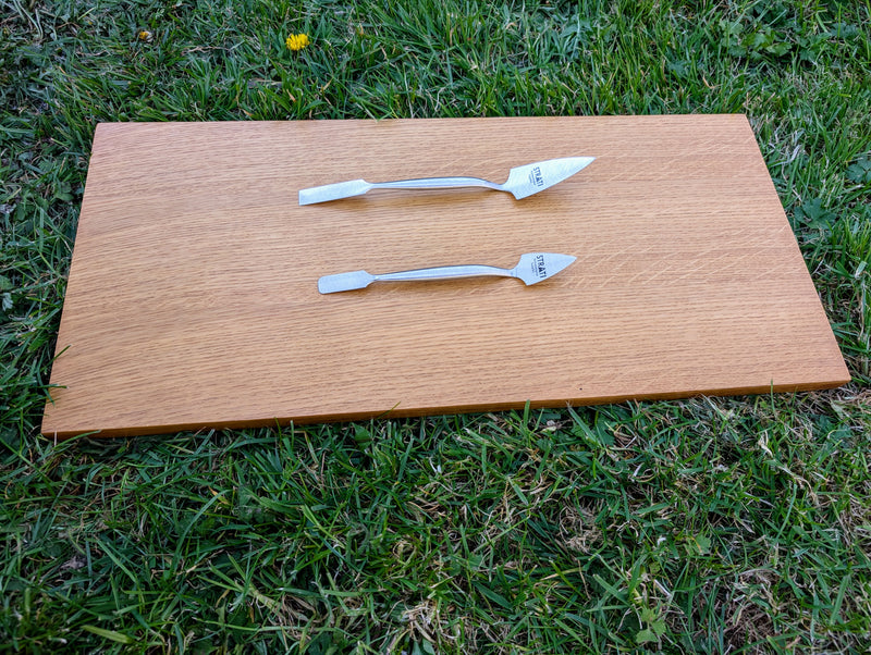 Load image into Gallery viewer, Top profile view of two forged stainless steel spatulas on light wood board over green grass