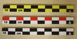 Three flat 10cm photo scales in RWB, BW and BY color variants on beige surface. Compact size for small artifact documentation.