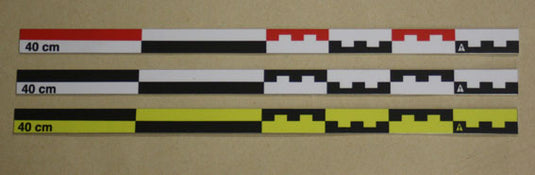 Three flat 40cm archaeological photo scales laid flat on beige background: red-white-black (top), black-white (middle), black-yellow (bottom). Aluminum body. Made in France.