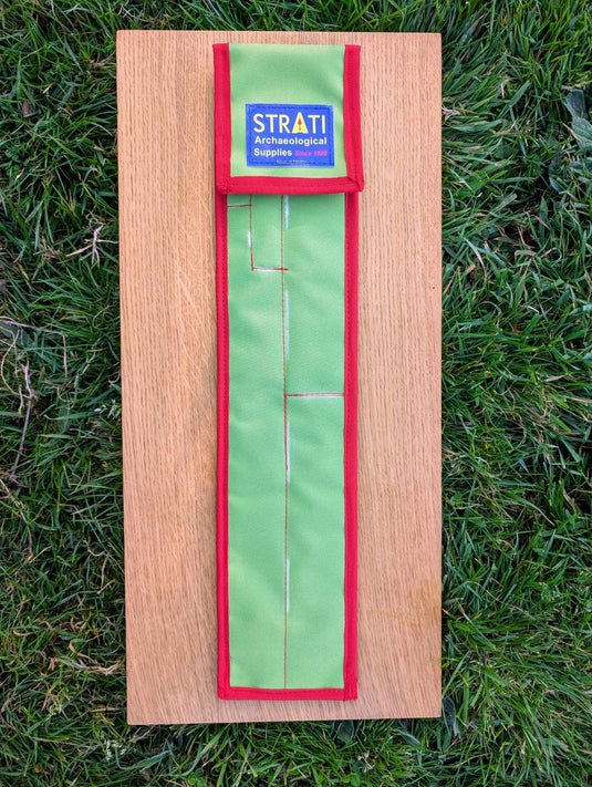 Closed CAMA 50 cm green and red carrying case for archaeological photo scales on wooden board over grass