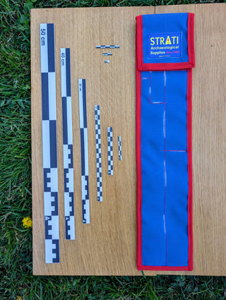 Chargez l'image dans la visionneuse de la galerie, CAMA 50 cm black and white archaeological photo scale set with STRATI blue and red case on wood and grass
