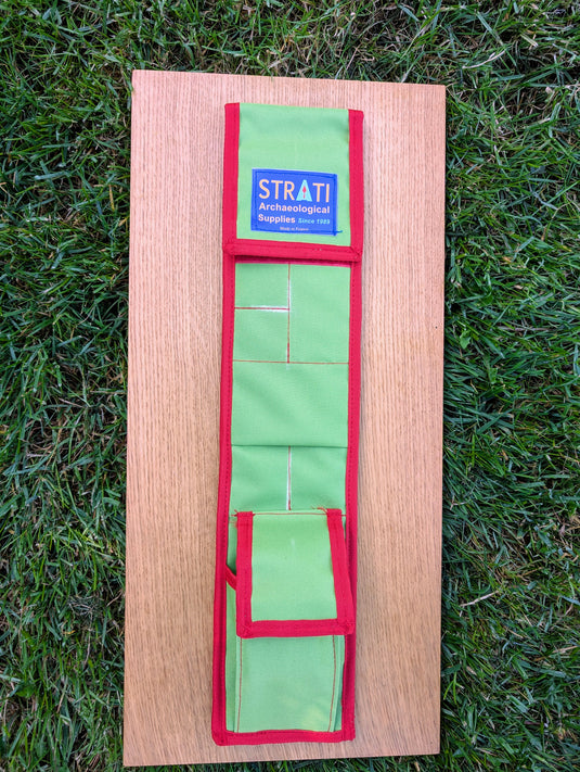 Open green and red CANVAS 50 cm STRATI roll-up case with organized pockets on light wood over grass