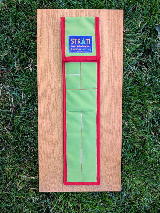 Closed CANOMA 50 cm green and red STRATI carrying case for archaeological photo-scale kit on wood over grass