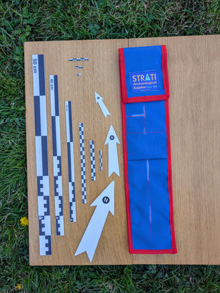 Chargez l'image dans la visionneuse de la galerie, CANOMA 50 cm black-white archaeological scale set with north arrows and open blue-red case on wood and grass
