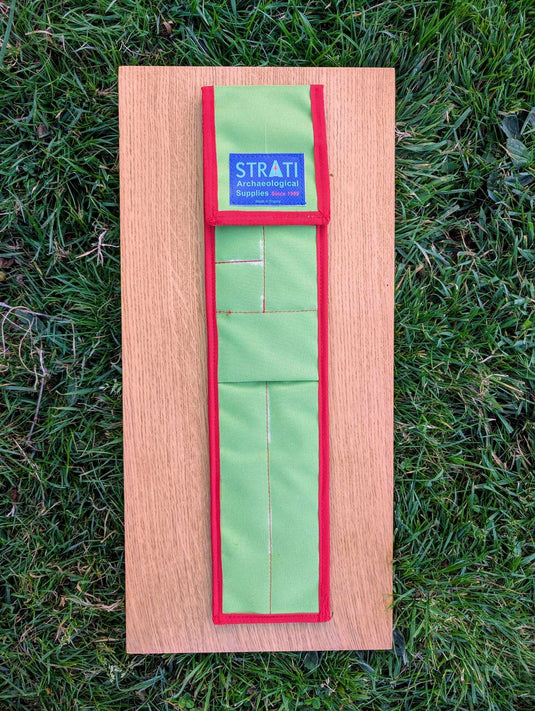 Closed CANO 50 cm green and red STRATI carrying case for archaeological photo-scale kit on wood over grass