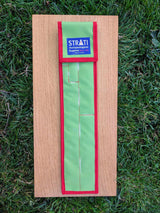 Closed green and red STRATI CASE carrying case for archaeological photo scales on a wooden board over grass