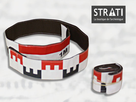 Flexible 1m CANVAS photo scale tape shown unrolled in a loop and rolled up compactly. White fabric with red and black metric markings. Reverse side is black stitched fabric.