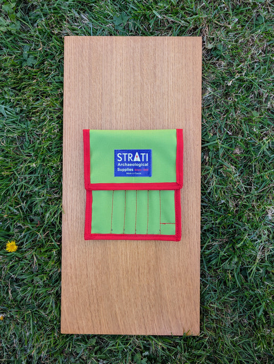 Closed green Strati tool case for precision tweezers on a wooden board and grass background