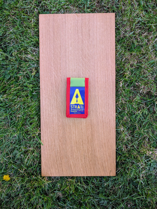 Closed Strati Minimix+ red-white-black archaeology photo-scale pouch with green and red fabric on wood over grass