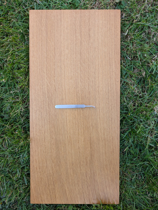 110 mm straight stainless steel precision tweezers on light oak wood board over green grass