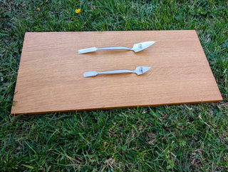 Chargez l'image dans la visionneuse de la galerie, Top profile view of two forged stainless steel spatulas on light wood board over green grass

