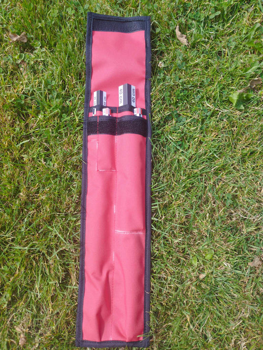 Red-white-black angular archaeological photo scales in an open red and black fabric holder on grass