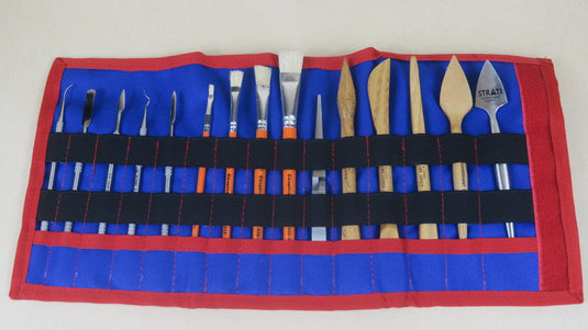 Open red and blue SCADS three-section tool roll with sculpting tools, metal picks and brushes on beige background