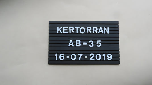 Small black grooved archaeological letter board with white removable letters and numbers on a light background